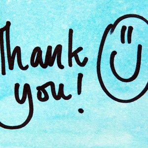 May include: A handwritten message on a light blue watercolor background. The words "Thank you!" are written in black ink, accompanied by a smiling face. The design is simple and cheerful, perfect for expressing gratitude.