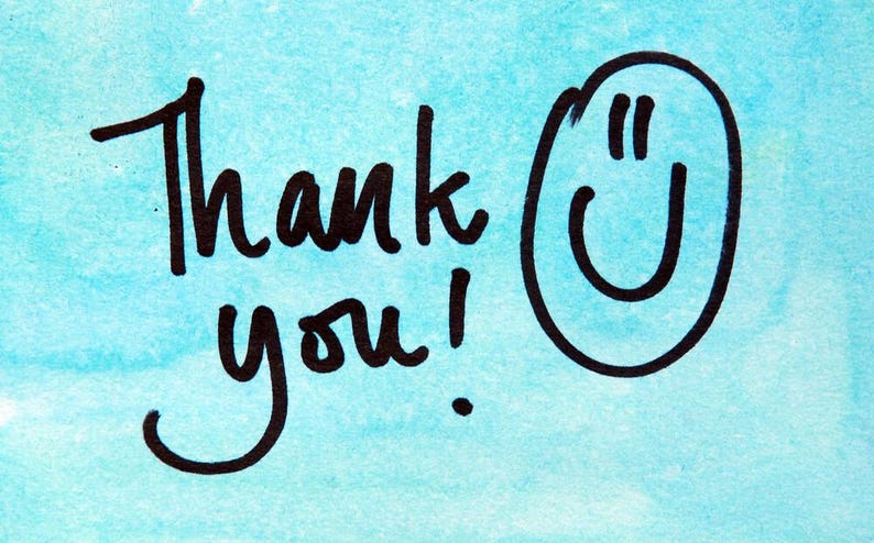 May include: A handwritten message on a light blue watercolor background. The words "Thank you!" are written in black ink, accompanied by a smiling face. The design is simple and cheerful, perfect for expressing gratitude.