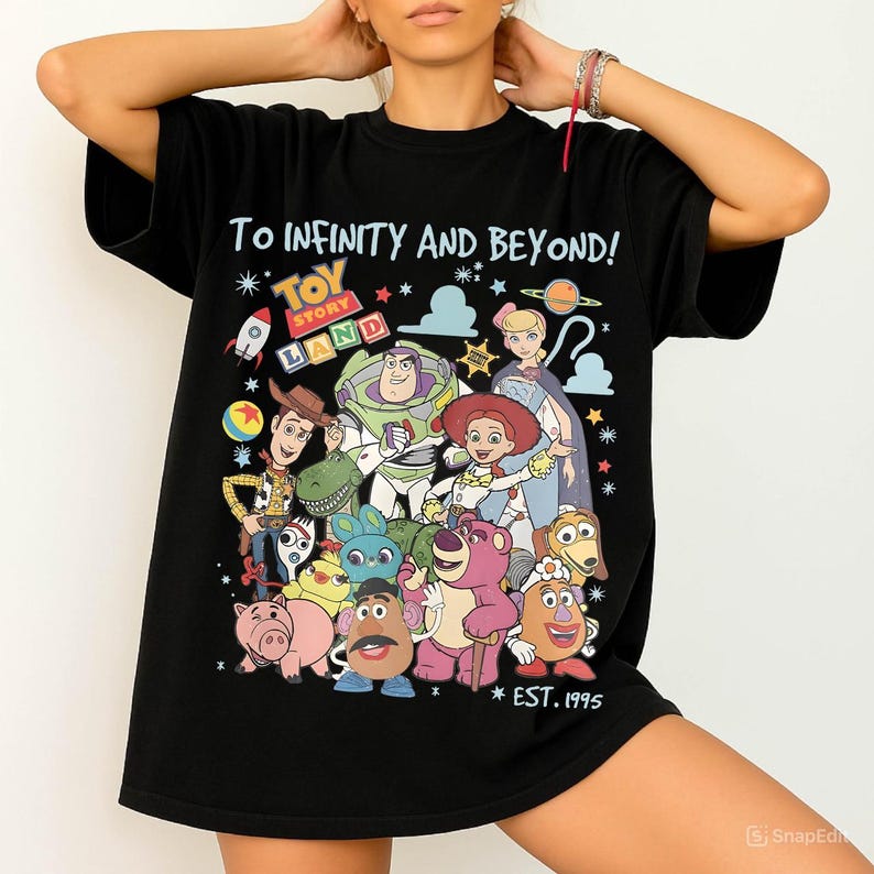 May include: Black t-shirt featuring a colorful graphic of Toy Story characters, including Woody, Buzz Lightyear, and Jessie. The shirt has the text "TO INFINITY AND BEYOND!" and "TOY STORY LAND" with "EST. 1995" below the characters.