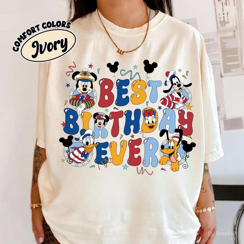 May include: Ivory-colored t-shirt with the words "BEST BIRTHDAY EVER" in colorful bubble letters. The design includes cartoon characters like Mickey Mouse, Minnie Mouse, Donald Duck, Goofy, and Pluto. The shirt has a Comfort Colors label.
