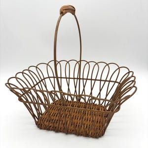 May include: A rectangular basket featuring a woven brown base and a wire frame with a scalloped upper edge. The basket includes a single tall, thin wire handle that is wrapped with a brown material at the top center for a comfortable grip.