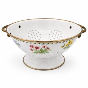 May include: White enamel colander with floral designs and brass-colored trim. The colander features a pedestal base and two handles. The floral pattern includes red, yellow, and blue flowers with green leaves. The colander has small holes for draining.