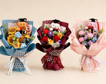 May include: Three bouquets of crocheted flowers and teddy bears, wrapped in blue, burgundy, and pink paper. Each bouquet features a teddy bear wearing a graduation cap and holding a diploma. The flowers include sunflowers, roses, and other colorful blooms.
