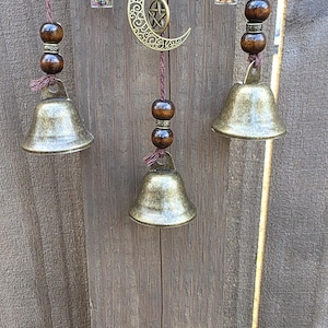 Side angle view of handmade protection witch bells with bronze bells, charms, and beaded details on a wooden background.
