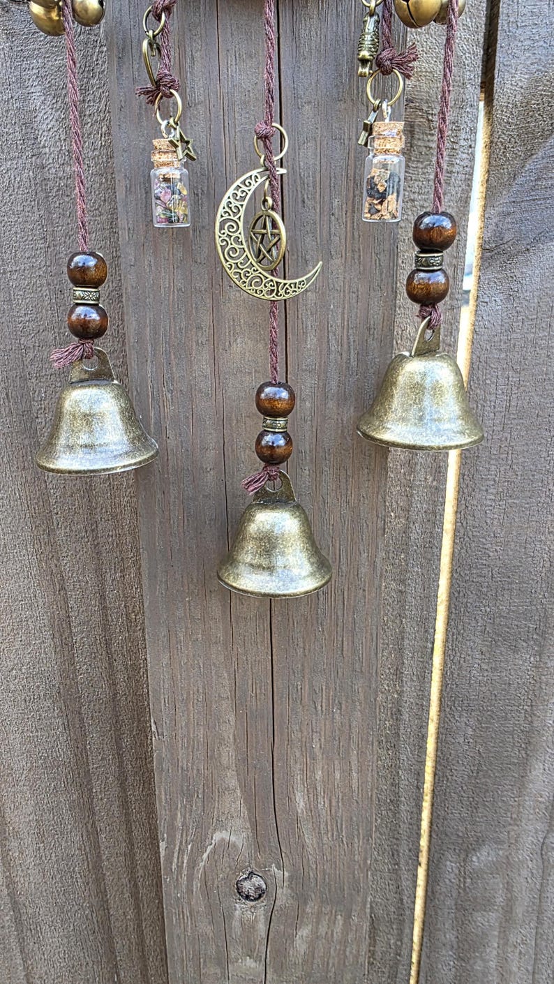 Side angle view of handmade protection witch bells with bronze bells, charms, and beaded details on a wooden background.
