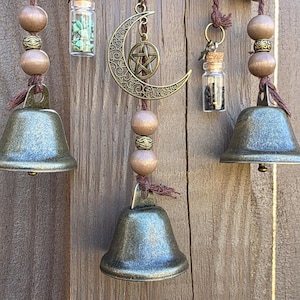 Close-up of witch bell charms including a crescent moon, tree of life, gemstones, and protection vials on braided cord