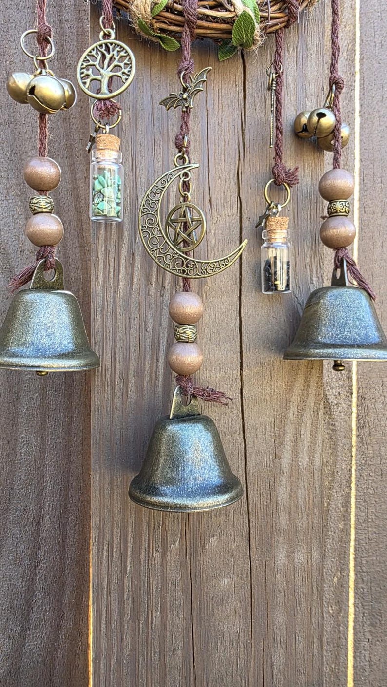 Close-up of witch bell charms including a crescent moon, tree of life, gemstones, and protection vials on braided cord