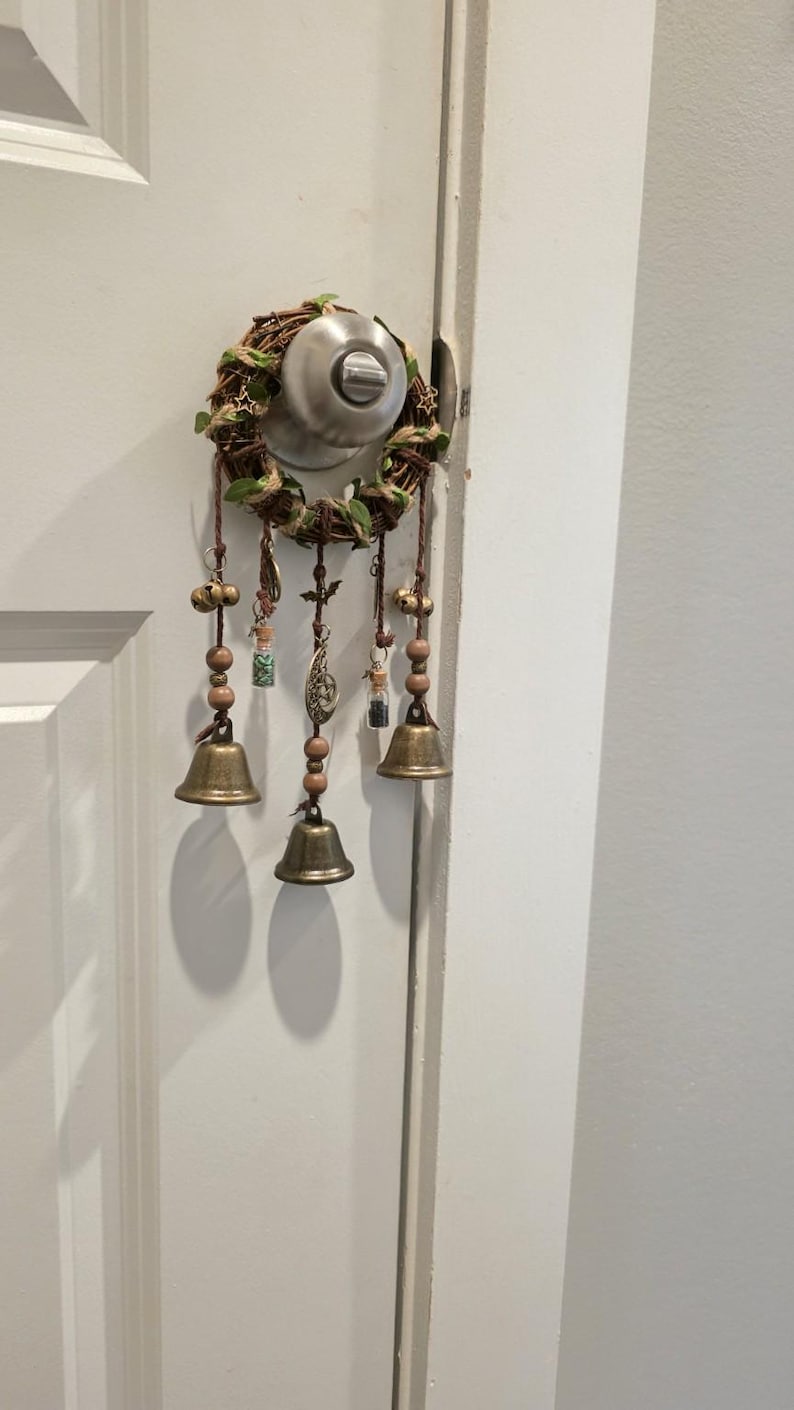 Witch bells hanging on a door handle as protective home décor, featuring bronze bells, charms, and gemstone vials