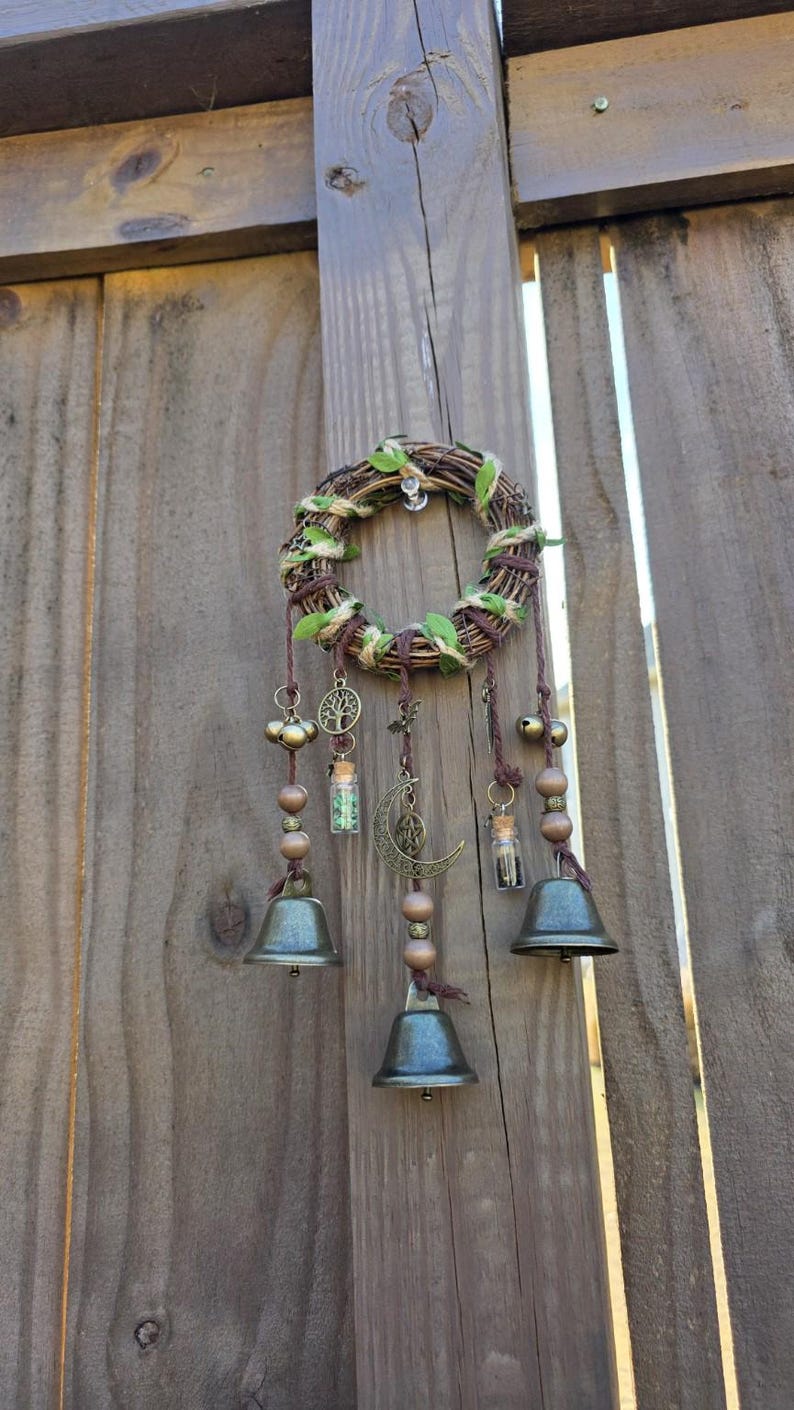 Handcrafted witch bells hanging on a wooden fence, featuring bronze bells, charms, and gemstone vials for home protection décor.