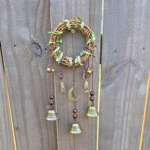 Side angle view of handmade protection witch bells with bronze bells, charms, and beaded details on a wooden background.