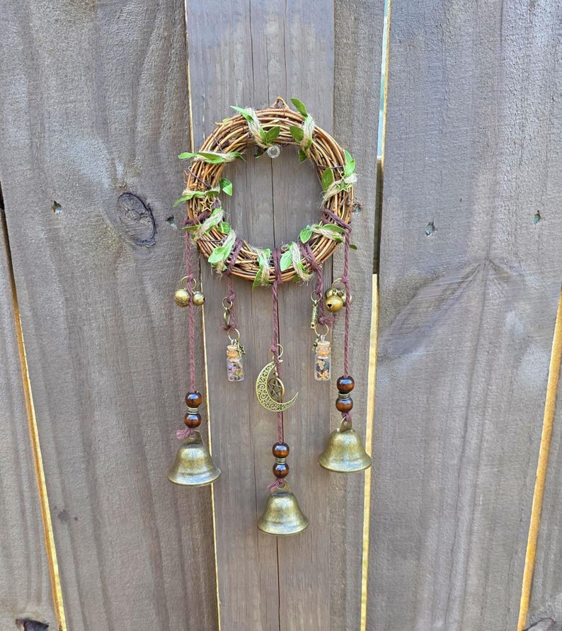 Side angle view of handmade protection witch bells with bronze bells, charms, and beaded details on a wooden background.