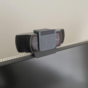 Puede incluir: Una webcam Logitech negra y gris montada en un monitor de ordenador. La webcam tiene un micrófono incorporado y está etiquetada como "HD 1080p". Está diseñada para videoconferencias y streaming.