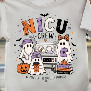 Può includere: Una t-shirt bianca con una grafica che riporta il testo NICU CREW e WE CARE FOR THE SMALLEST MIRACLES. Il design include tre fantasmi, un neonato in un'incubatrice, una zucca e una pila di libri con le etichette tiny patients, big hearts, endless impact.