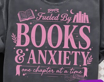 May include: A charcoal gray crewneck sweatshirt featuring a pink graphic print that reads Fueled By BOOKS & ANXIETY one chapter at a time. The design includes illustrations of an open book, eyeglasses, a crescent moon, and a library due date stamp.