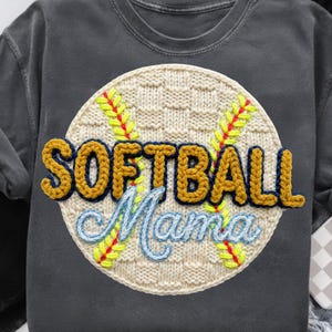May include: Dark grey sweatshirt with a large, textured patch. The patch features a softball design with the words "SOFTBALL Mama" in yellow and blue stitched lettering. The softball design includes yellow and red stitching.