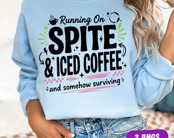 May include: A light blue crewneck sweatshirt featuring black text that reads Running On SPITE & ICED COFFEE and somehow surviving. The design includes a small coffee cup icon, lime green starbursts, and pink checkered accents with horizontal lines.
