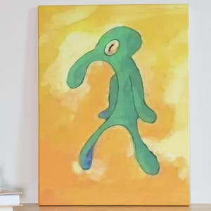 May include: A canvas print featuring a stylized, green figure with a long nose and one eye, set against a yellow and orange background. The artwork is displayed on a wooden table next to a stack of books.