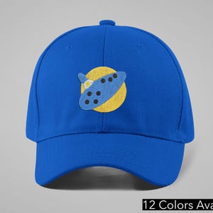 May include: A royal blue baseball cap with a curved brim. The cap features a patch of a blue and yellow cartoon design. The text "12 Colors Available" is at the bottom of the image.