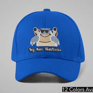May include: A royal blue baseball cap featuring an embroidered cartoon Blastoise character wearing sunglasses. The text "Big Man Blastoise" is below the character. The cap has a curved brim and a button on top. The text "12 Colors Available" is at the bottom.