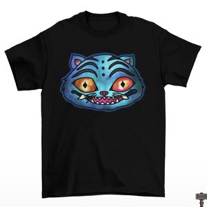 May include: Black t-shirt featuring a blue cat face graphic. The cat has orange eyes, a pink mouth, and white fangs. The cat's face has blue stripes and is outlined in black. The graphic is centered on the front of the shirt.