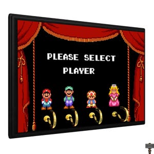 May include: Black framed key holder featuring a retro video game design. The design includes the text "PLEASE SELECT PLAYER" above pixelated characters. Four gold-colored hooks are below the characters. Red curtains frame the design.