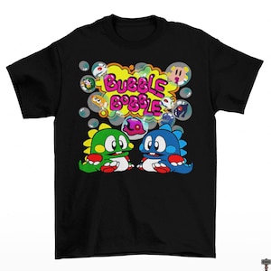 May include: Black t-shirt featuring a colorful graphic from the video game Bubble Bobble. The design includes two dinosaur-like characters, bubbles, and the game's logo in a yellow bubble. The characters are green and blue.
