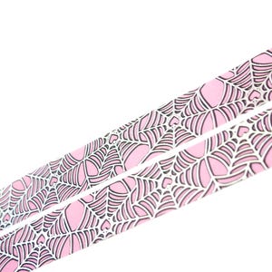 May include: Pink and white washi tape with a spiderweb pattern. The tape has a holographic finish.