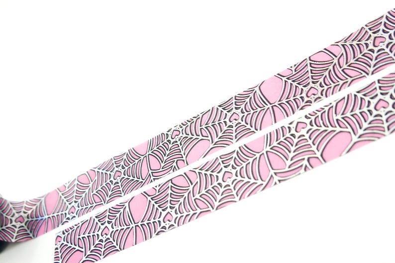 May include: Pink and white washi tape with a spiderweb pattern. The tape has a holographic finish.