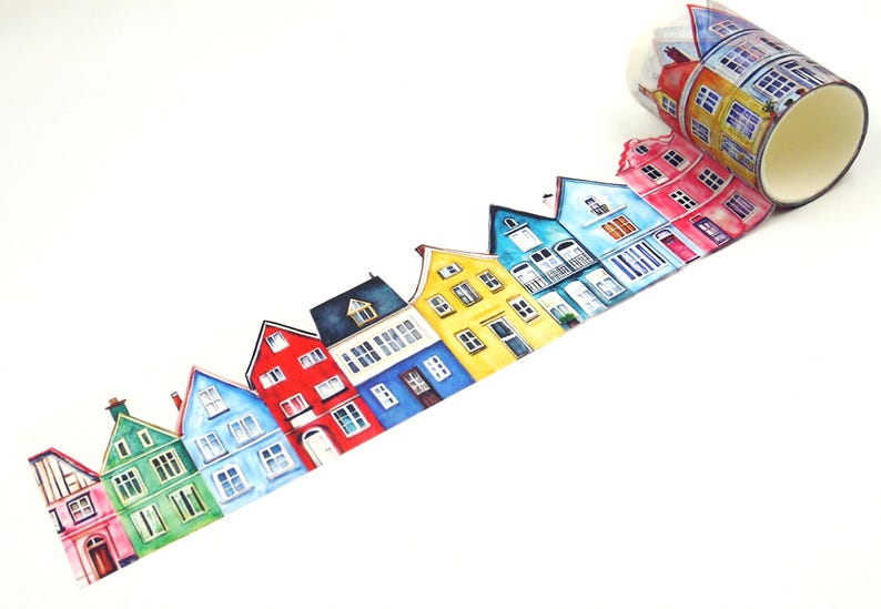 May include: A roll of decorative washi tape featuring a colorful illustration of quaint houses. The houses are painted in various colors, including green, blue, red, and yellow, with detailed windows and architectural features. The tape is unrolled, showing the repeating pattern.