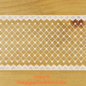 Puede incluir: Ribete de encaje blanco con un patrón de diamantes sobre un fondo marrón claro. El encaje tiene un borde festoneado. El texto "Etsy's Happy Zakka Life" está en naranja en la parte inferior de la imagen.