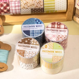 Könnte beinhalten: Vier Rollen dekoratives Washi-Tape mit Patchwork-Designs. Jede Rolle hat ein anderes Muster, darunter blauer Denim, rotes Karomuster und Blumendrucke. Der Text "PATCHWORK NOTES" ist auf jeder Rolle aufgedruckt.