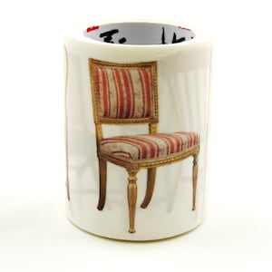 Puede incluir: Rollo de cinta adhesiva washi cilíndrica blanca con una ilustración detallada de una silla clásica. La silla tiene un marco dorado y un asiento con rayas verticales rojas y blancas. El diseño de la cinta evoca una estética vintage y antigua.