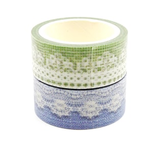 Può includere: Due rotoli di nastro adesivo decorativo. Il rotolo superiore è verde con un motivo a pois e pizzo bianco. Il rotolo inferiore è blu con un motivo a pizzo bianco. Il nastro è impilato.