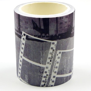 Pode incluir: Um rolo de fita adesiva decorativa com um design de tira de filme em preto e branco. A fita apresenta um fundo de paisagem urbana e detalhes de moldura de filme. A fita é cilíndrica com um interior amarelo claro.