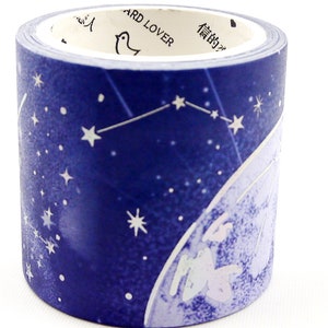 Op de afbeelding: Een rol decoratieve washi-tape met een donkerblauw nachthemelontwerp met witte sterren en sterrenbeelden. De tape heeft een hemels thema, met een maan en een figuur. De binnenrol heeft tekst en een vogelillustratie.