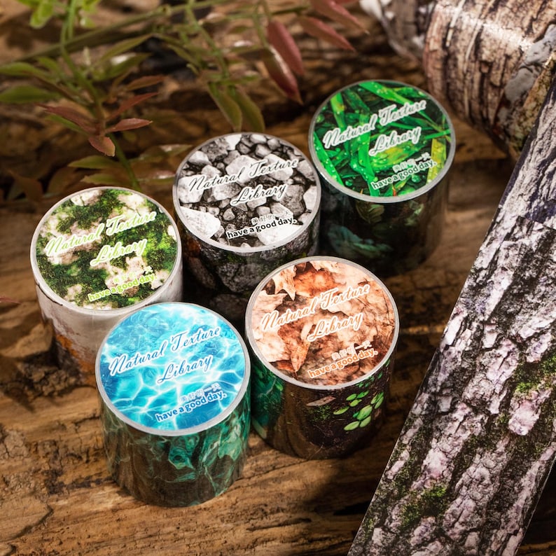 Peut inclure: Plusieurs rouleaux de ruban adh&eacute;sif washi d&eacute;coratifs avec des motifs sur le th&egrave;me de la nature. Chaque rouleau pr&eacute;sente un motif diff&eacute;rent, notamment des roches, de l'eau, des feuilles et de l'&eacute;corce. Le texte "Natural Texture Library" et "have a good day" est imprim&eacute;.