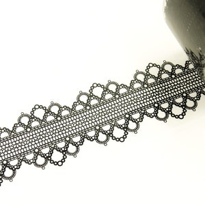 Puede incluir: Un rollo de cinta washi negra con un delicado patrón de encaje. La cinta está parcialmente desenrollada, revelando el diseño de encaje negro.