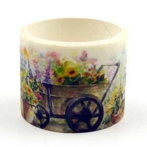 May include: Washi tape roll with a watercolour illustration of a garden scene. The design features a wheelbarrow filled with sunflowers and other colourful flowers, with a butterfly. The tape is on a white background.