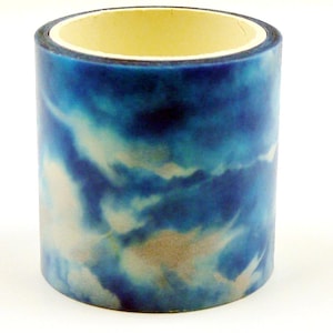 Könnte beinhalten: Eine Rolle dekoratives Washi-Tape mit einem Wolkenhimmel-Design. Das Klebeband weist Farbtöne von Blau, Weiß und Beige auf und erzeugt einen Aquarelleffekt. Das Klebeband ist zylindrisch mit einem gelben Innenkern.