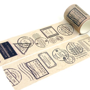 May include: A roll of brown washi tape featuring black ink stamps of various cities and countries, including Bangkok, Thailand, Berlin, Germany, Dubai, and Sydney, Australia. The tape has a vintage, travel-inspired design.