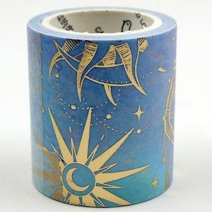 May include: A roll of decorative washi tape with a celestial design. The tape features a blue background with gold sun, moon, and star illustrations. The tape is approximately 3.8 cm wide.