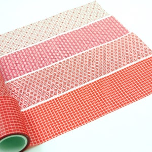 Könnte beinhalten: Dekorative Washi-Tape-Rollen und -Streifen in Rot- und Rosatönen. Die geometrischen Muster umfassen Gitter, Sterne und Blumen. Die Rollen sind teilweise abgerollt und zeigen die gemusterten Klebebänder.