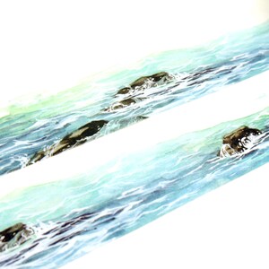 May include: A roll of washi tape with a watercolor design of ocean waves and rocks. The tape is light blue and green with brown rocks.
