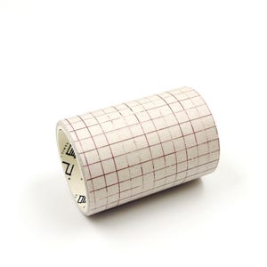 May include: A roll of transfer tape featuring a white background with a dark red grid pattern printed on the surface. The inner core of the roll is white and displays black text and symbols, including the word vinyl, along the inner edge.