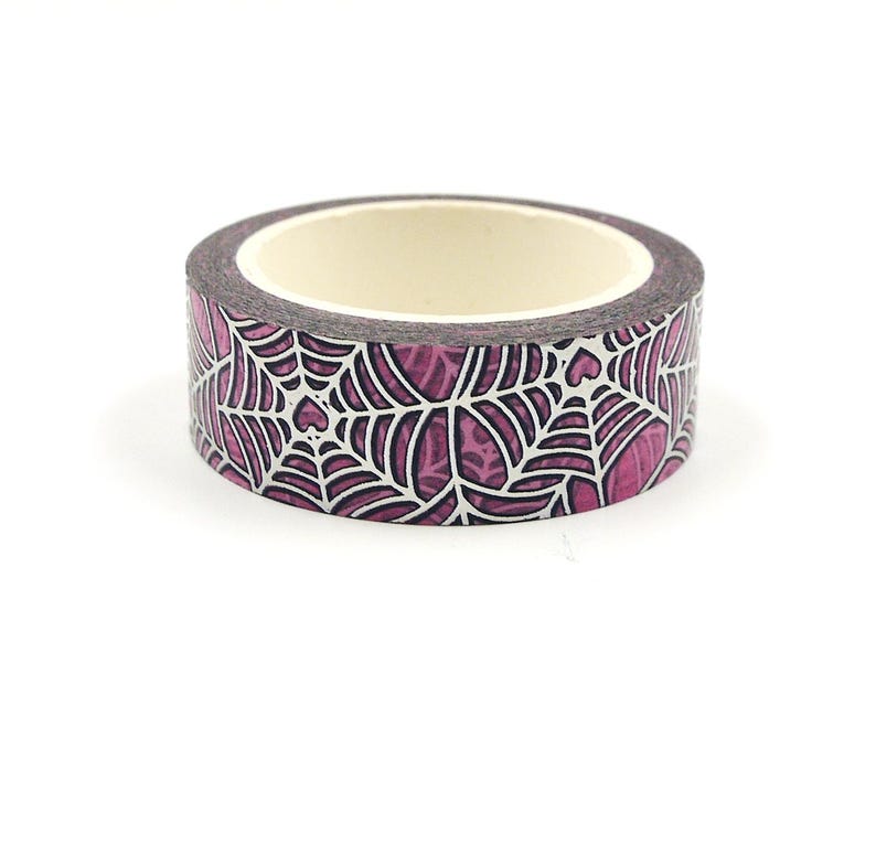 May include: A roll of pink and white washi tape with a spiderweb pattern. The tape has a white background with a pink spiderweb design.