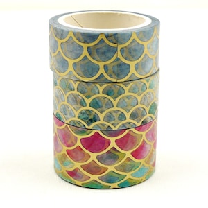 May include: Three rolls of washi tape with a gold and blue mermaid scale pattern. The top roll is blue, the middle roll is green, and the bottom roll is pink.