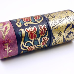 Pu&ograve; includere: Quattro rotoli di nastro washi decorativo con motivi dorati e floreali su sfondo blu scuro. Il nastro &egrave; arrotolato e impilato uno sopra l'altro.