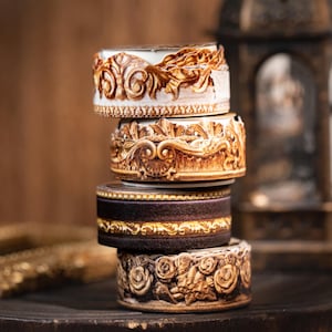May include: A stack of four decorative ceramic boxes. The boxes are in shades of brown and cream, with intricate floral and scrollwork designs. The boxes are stacked on top of each other, creating a visually appealing display.