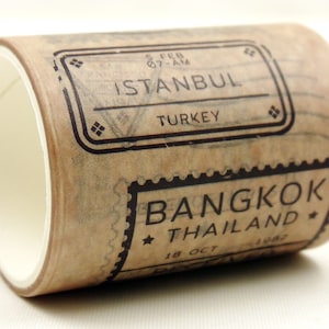 May include: A roll of brown washi tape with black stamps that say "ISTANBUL TURKEY" and "BANGKOK THAILAND".