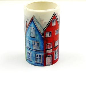 May include: A cylindrical washi tape roll featuring a watercolor illustration of colorful houses. The houses are painted in shades of blue, red, and green, with white window details. The tape is ideal for crafts and decorative projects.